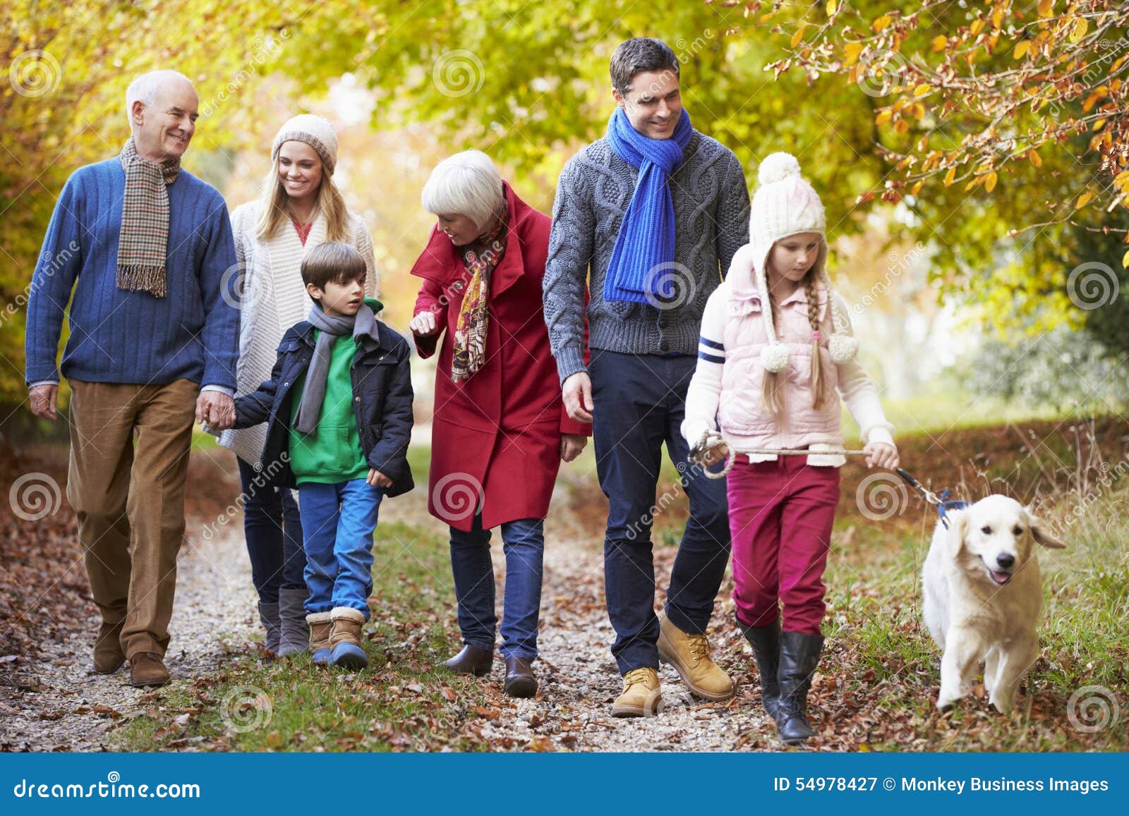 multl generation family walking along autumn path with dog