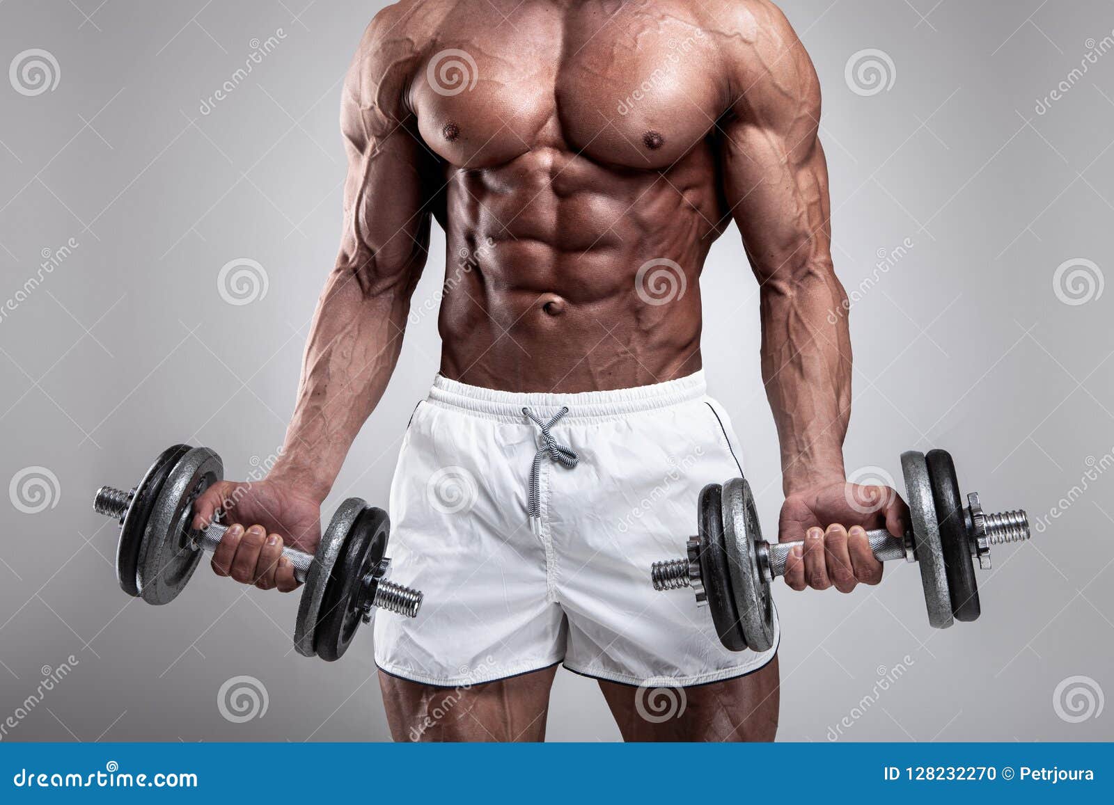 Muscular bodybuilder guy doing exercises with dumbbell over gray background