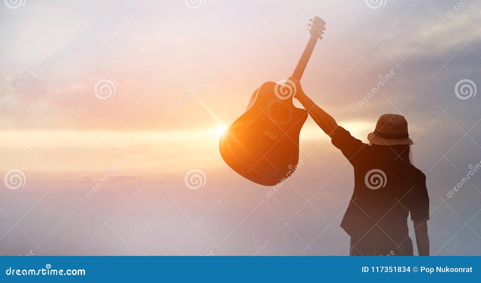 musician holding acoustic guitar in hand of silhouette on sunset