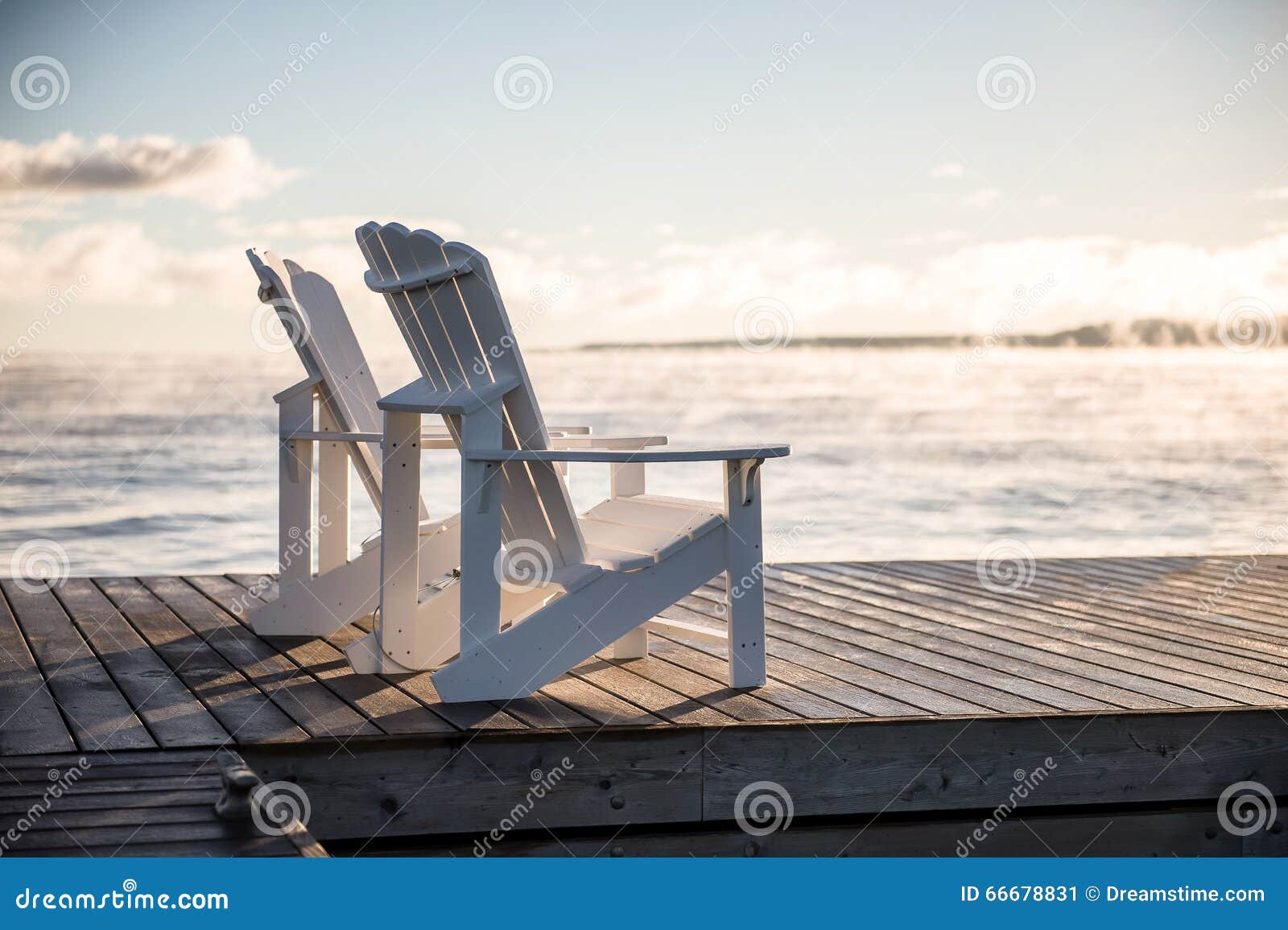 muskoka chairs on a dock with sun rising and mist