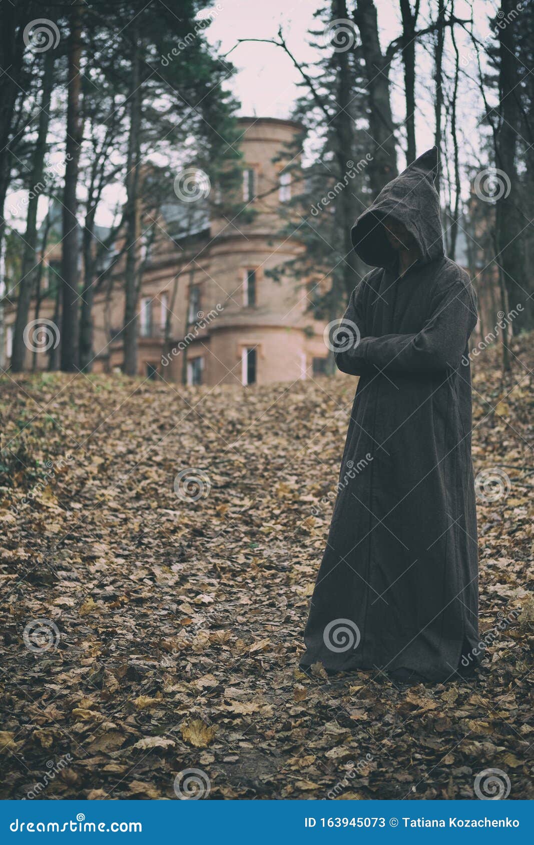mysterious monk, wizard or adept of secret society in hooded robe stands in forest against the background of medieval castle or
