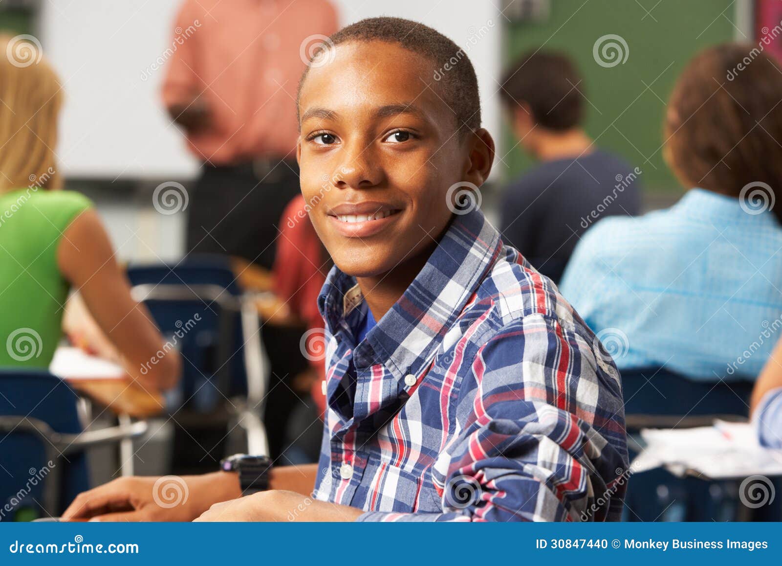 Männlicher Jugendschüler im Klassenzimmer, das an der Kamera unten lächeln sitzt