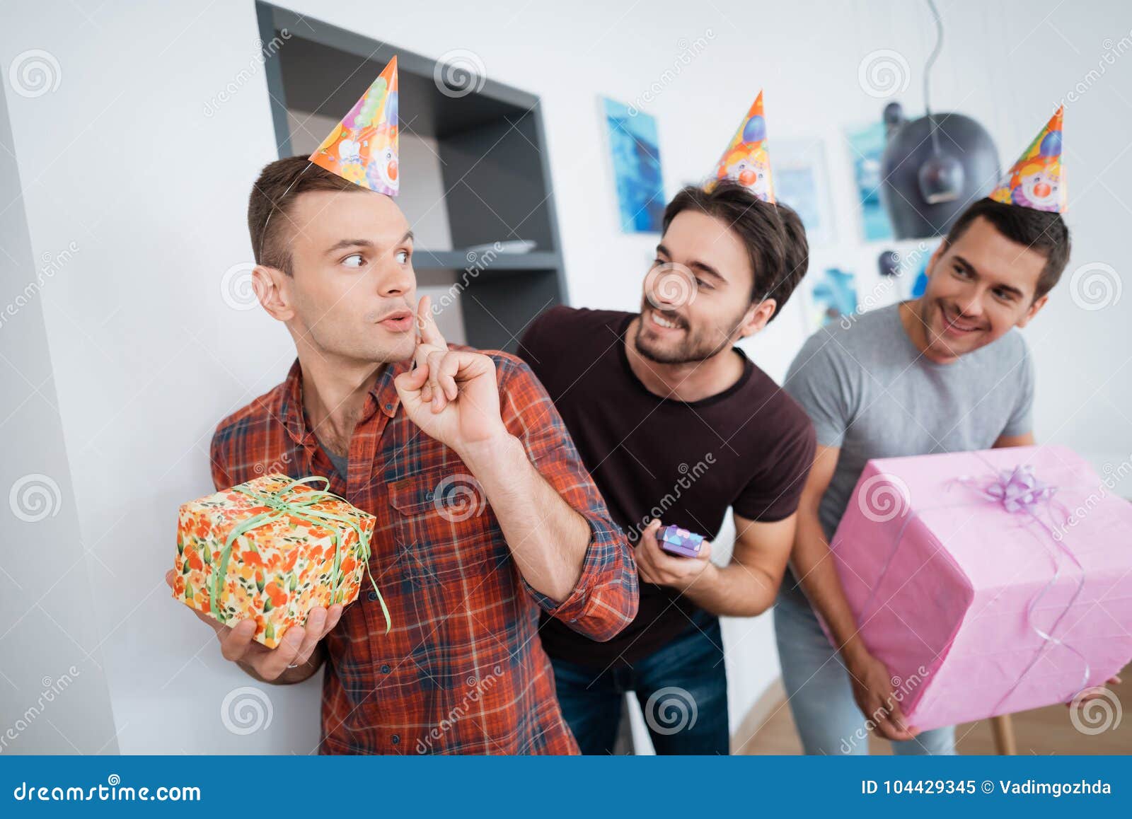 Mężczyzna w urodzinowych kapeluszach przygotowywają niespodzianki przyjęcia urodzinowego Przygotowywają spotykać urodzinowej dziewczyny Trzymają teraźniejszość w ich rękach