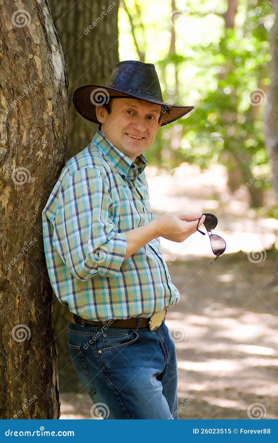 Przystojny uśmiechnięty mężczyzna z kowbojskim kapeluszem w lesie