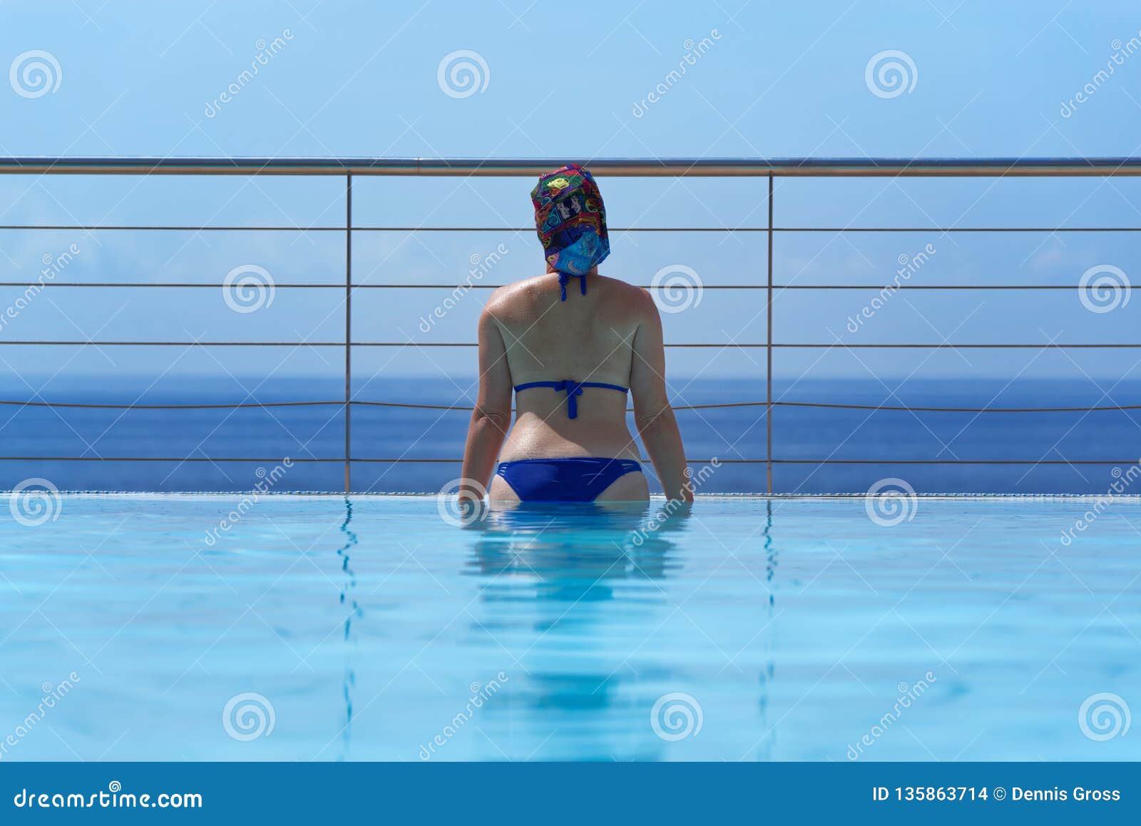 Młoda kobieta przy nieskończoność basenem patrzeje w kierunku horyzontu nad wodą