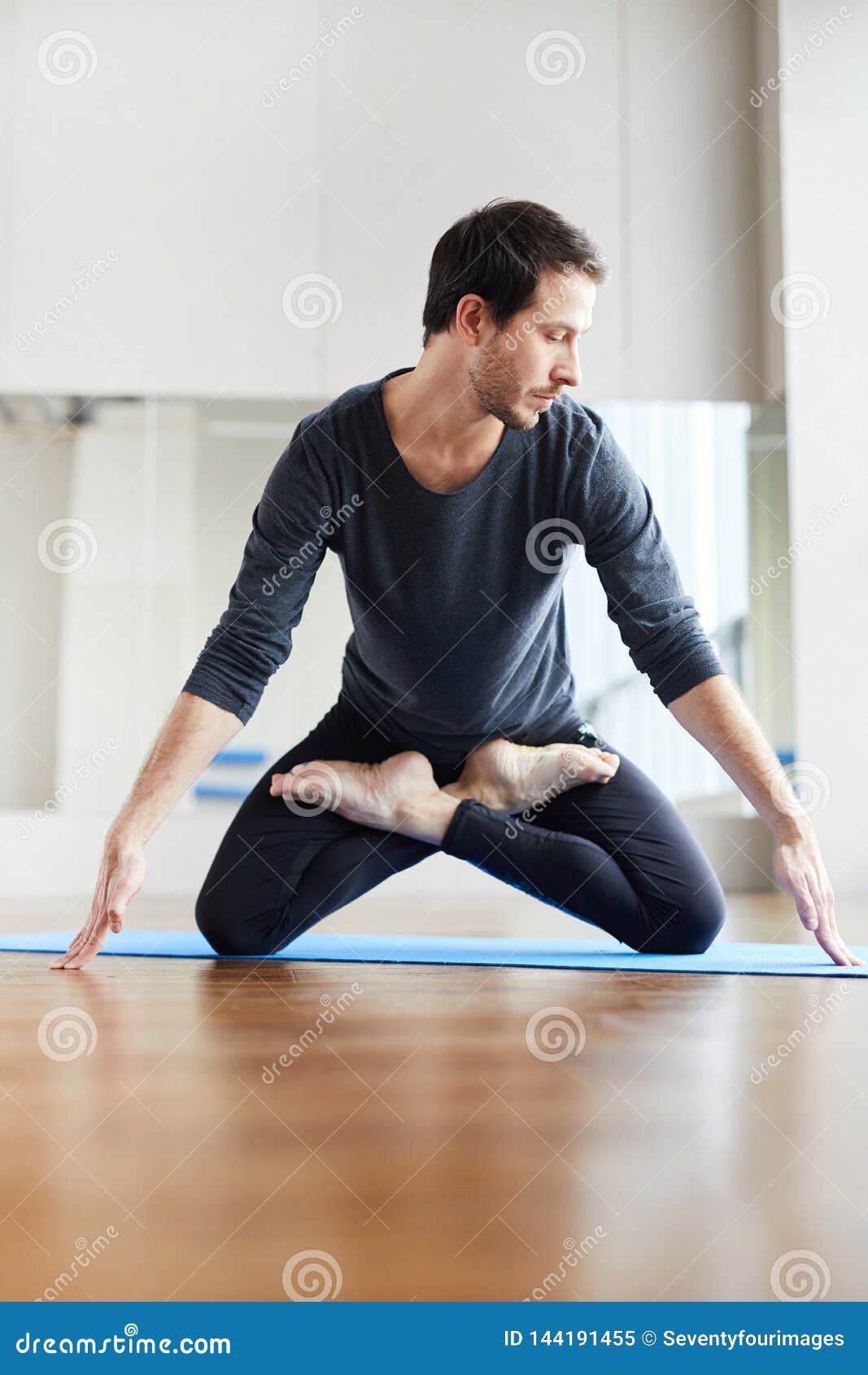 Młodzi yogis stoi na kolanach w lotosowej pozycji. Poważni przystojni młodzi yogis z ścierniskową pozycją na kolanach w lotosowej pozycji w joga studiu i opierać na palcach podczas gdy ćwiczący