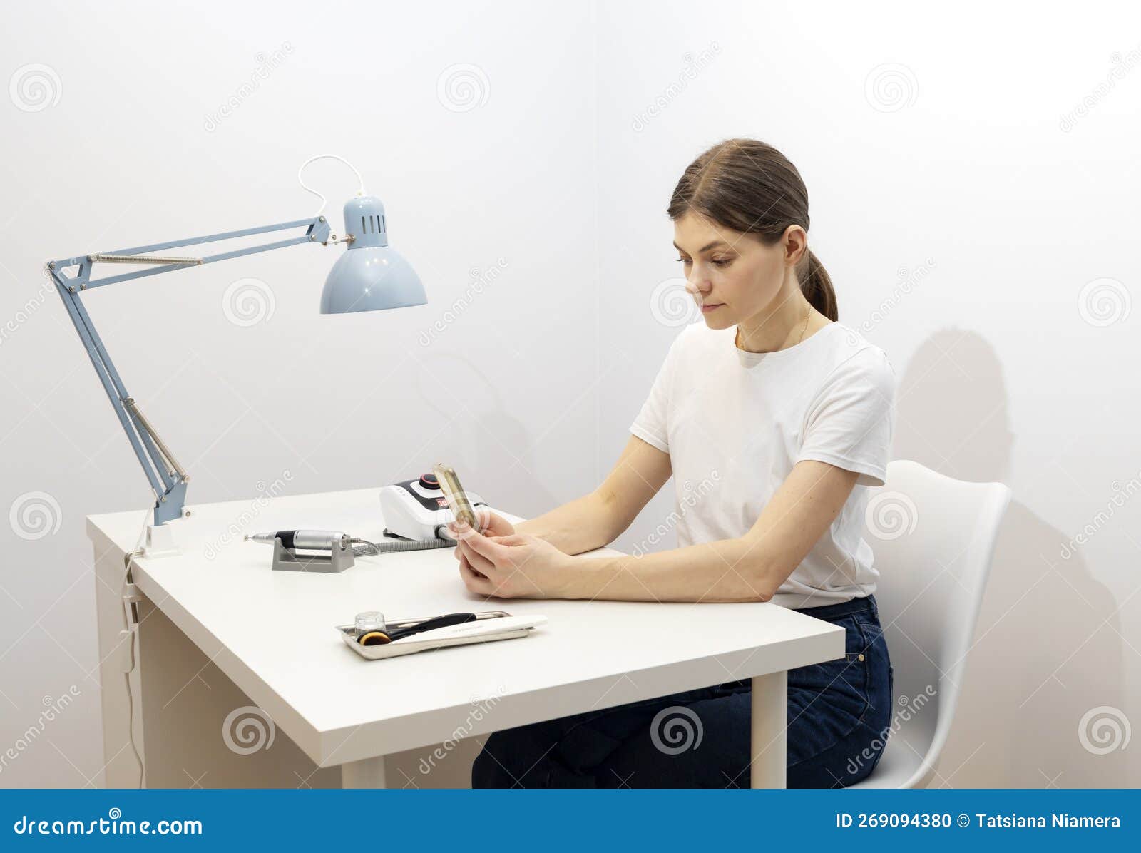 nail beautician hold gadget, looking at smartphone, sitting at workstation in nail beauty
