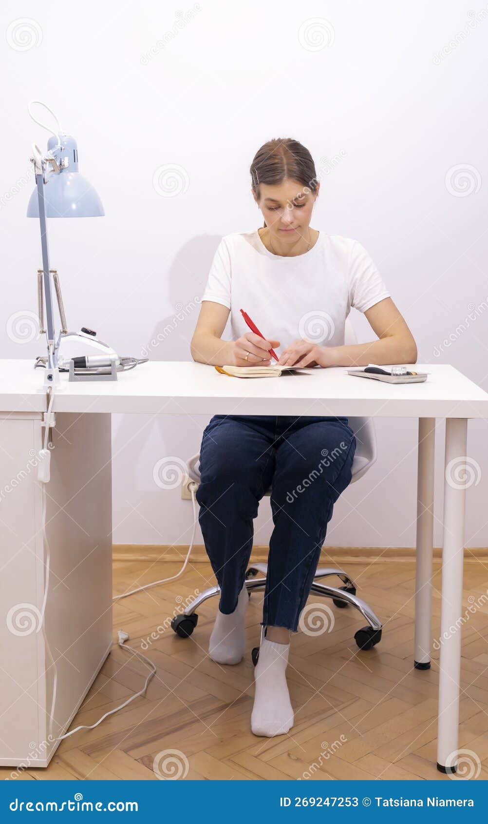 nail beautician makes notes in notebook with pen, sitting at workstation, table in