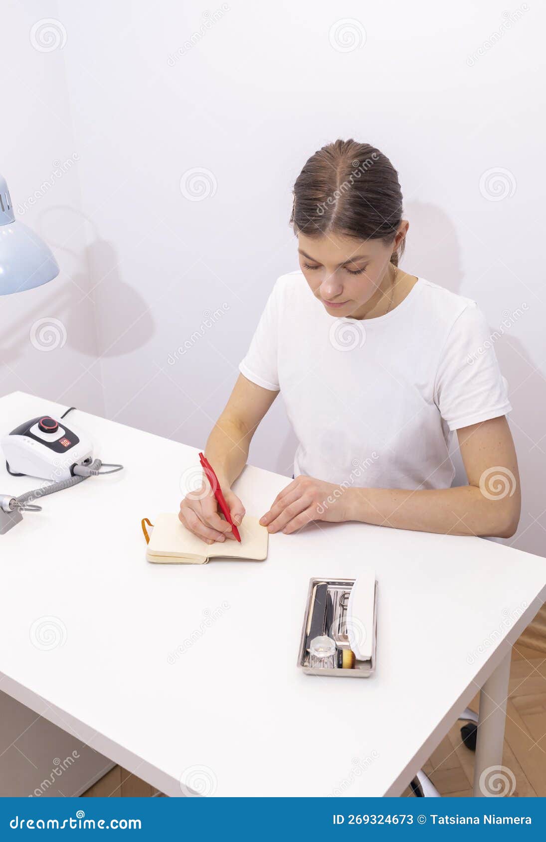 nail technician makes notes in notebook with pen, sitting at workstation, table in