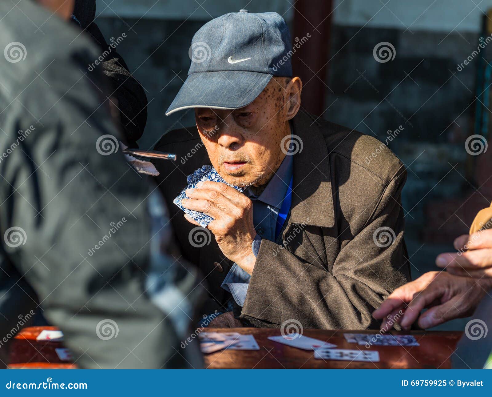 Naipes chinos mayores de los hombres en un parque en Pekín. Pekín, China - 15 de octubre de 2013: Retrato de los hombres chinos mayores que disfrutan de un juego de tarjetas con los amigos en los alrededores del Templo del Cielo en Pekín, China