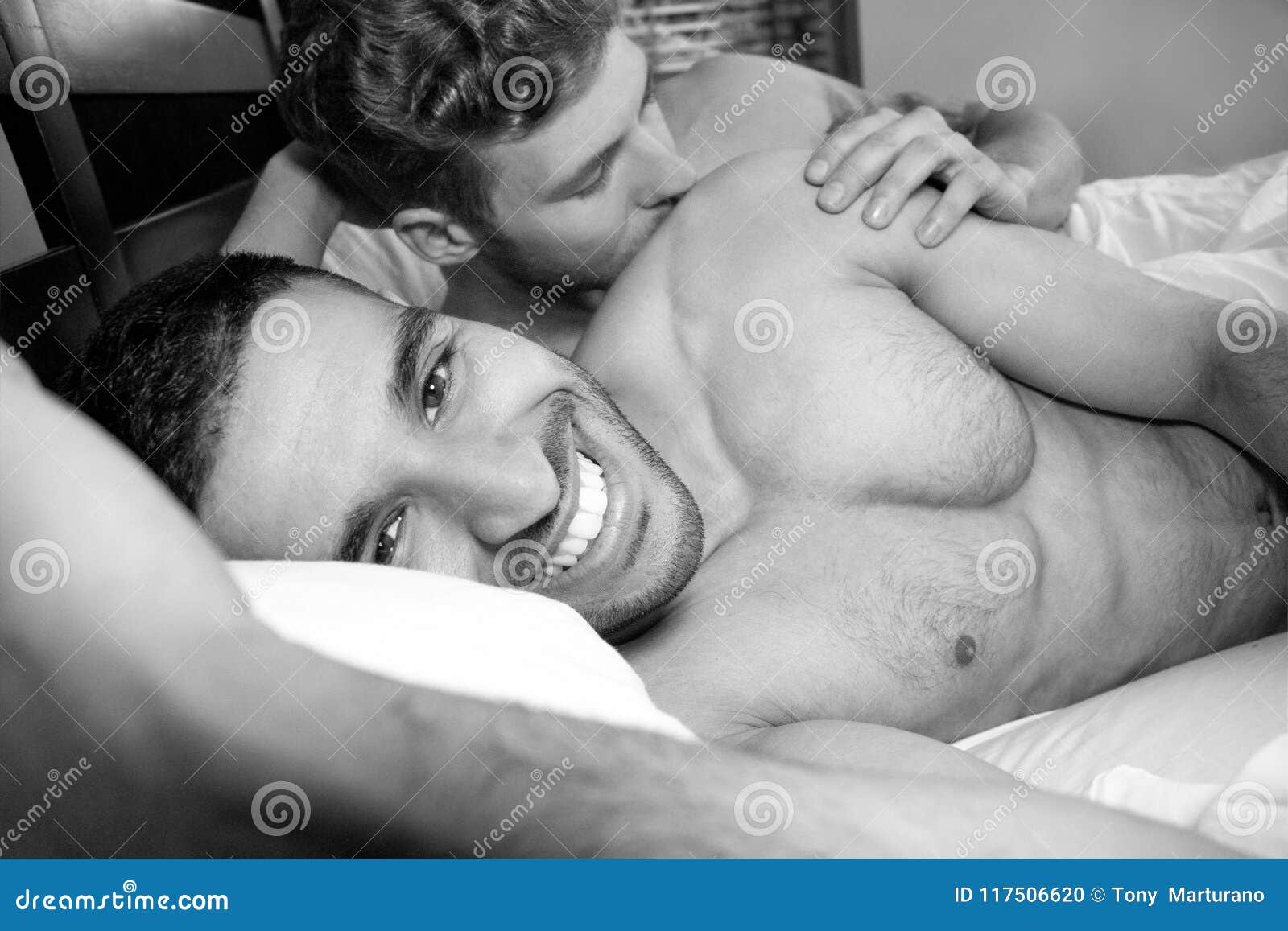 Photo about Two handsome gay men, nude in bed together cuddling and smiling...