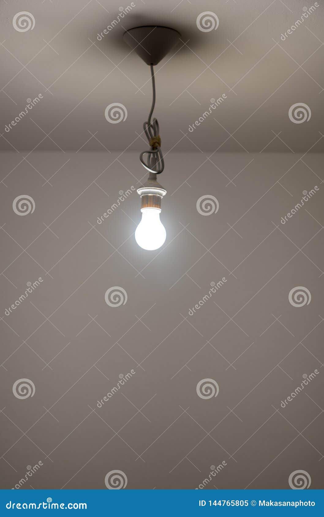 Naked Lit Light Bulb Hanging From The Ceiling Of A Dimly Lit Room