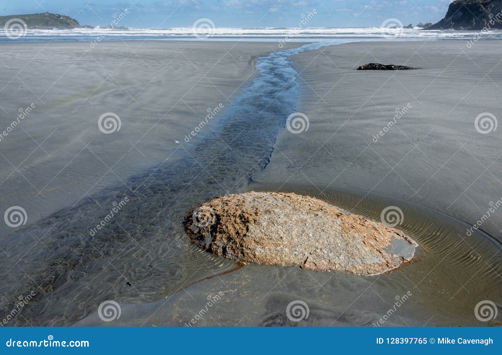 small stream flowing past exposed stone on deserted unspoiled beach