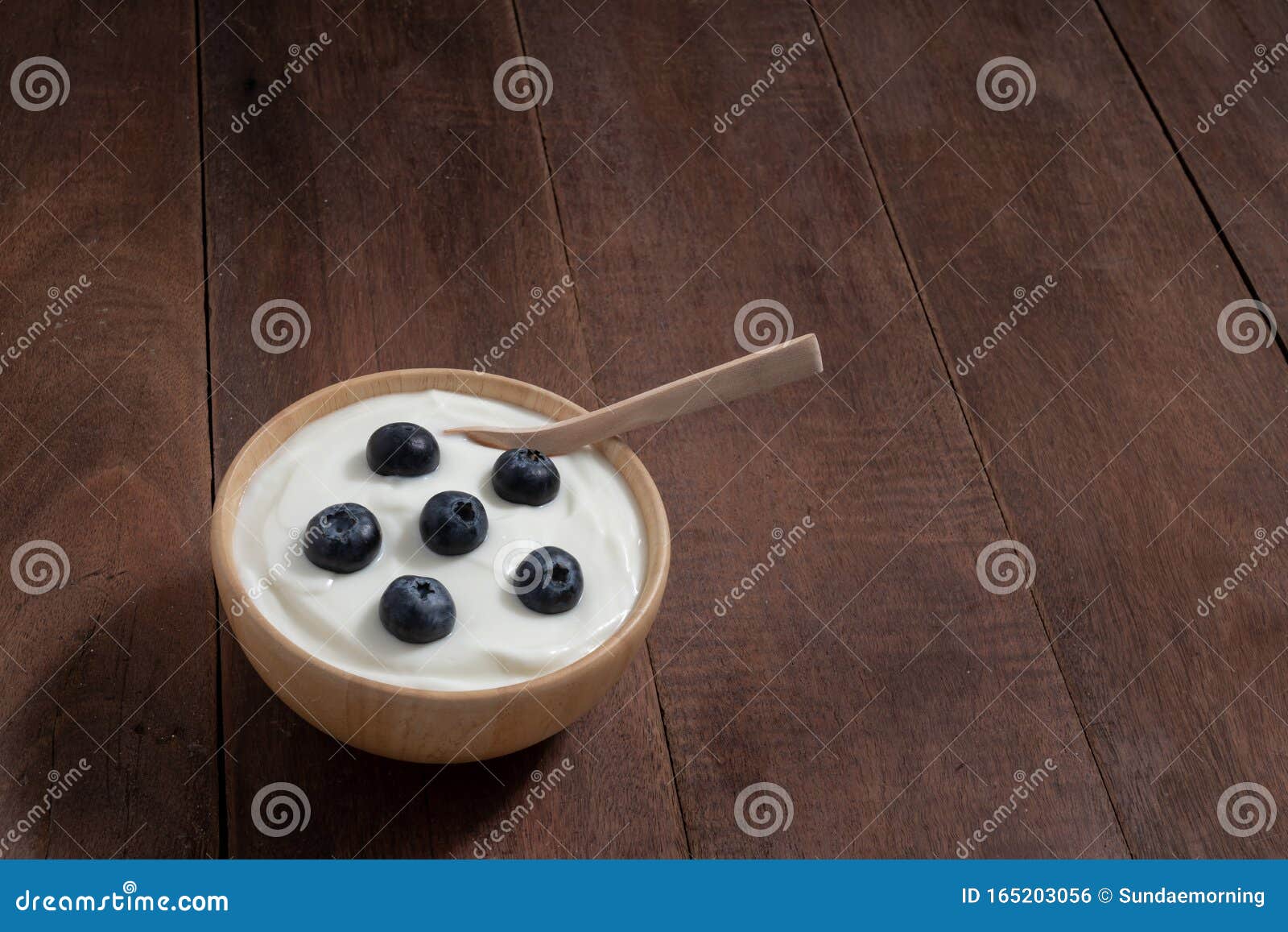 natural homemade plain organic yogurt mixed with fresh blueberry fruit in white bowl on wood texture background