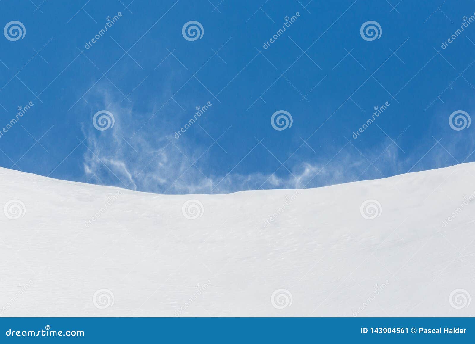 strong squall swirling snow in mountains, blue sky