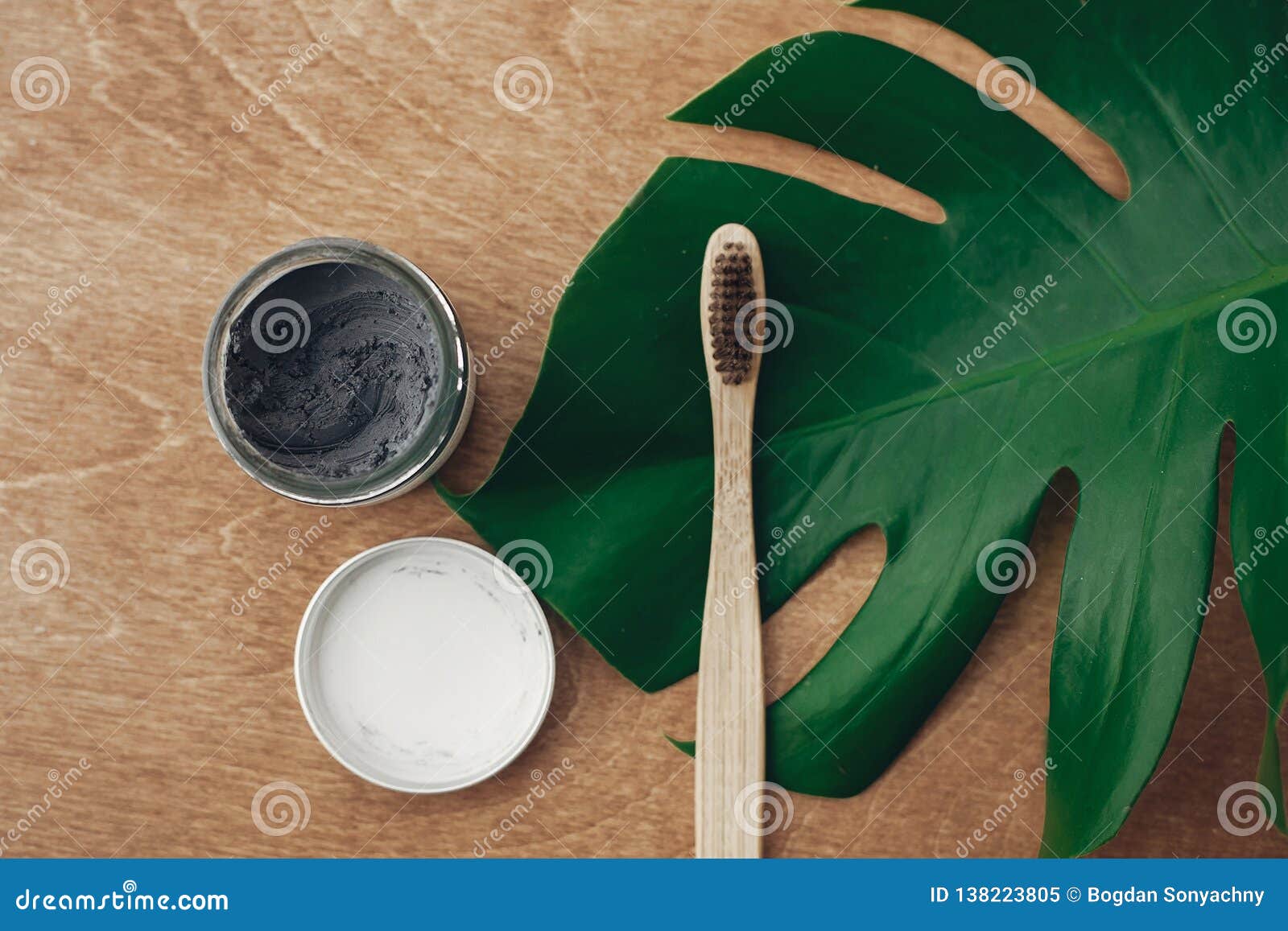natural toothpaste activated charcoal and bamboo toothbrush on wooden background with green monstera leaf. plastic free beauty