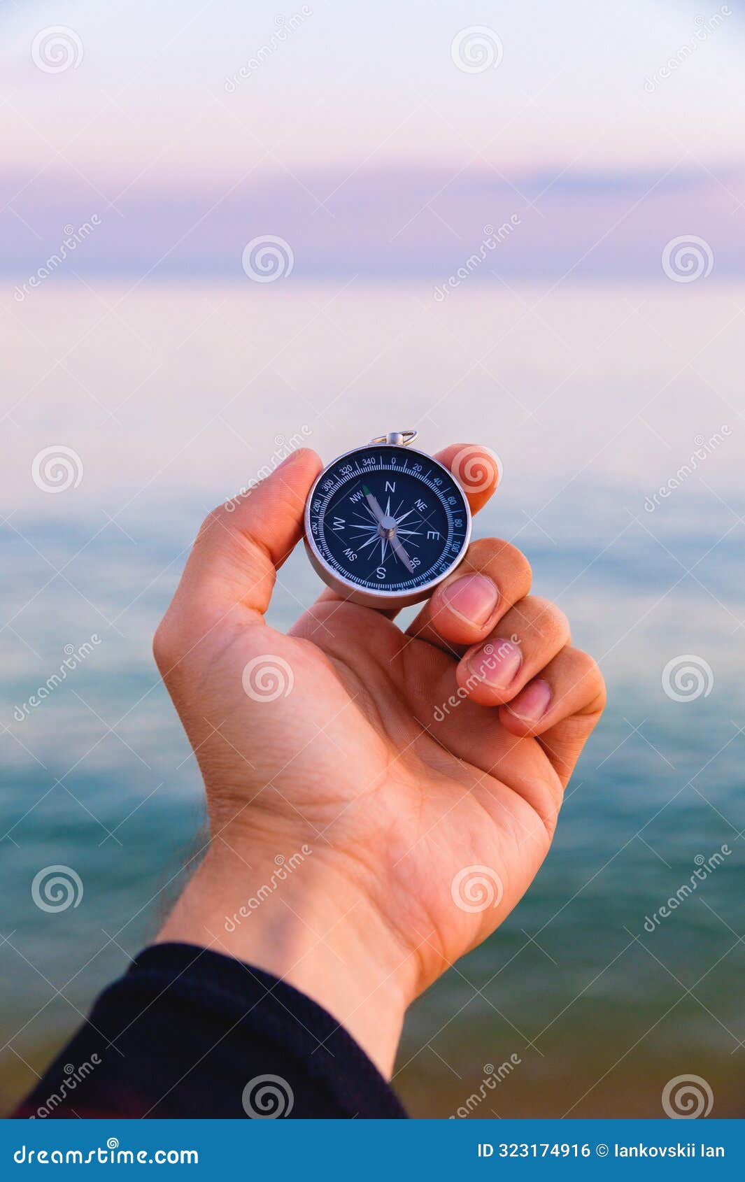 navigation compass in a man& x27;s hand against the background of the sea, tourist compass first person view