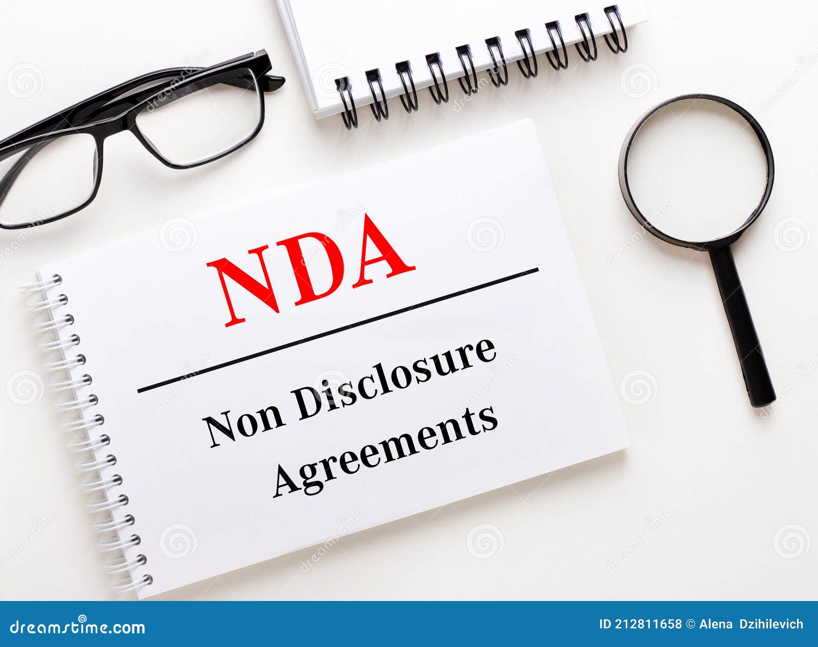 nda non disclosure agreements is written in a white notebook on a light background near the notebook, black-framed glasses and a