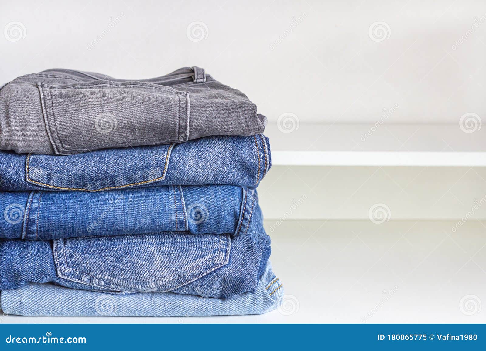 Neat Stack of Various Shades of Blue Jeans on a White Shelf. Clothes