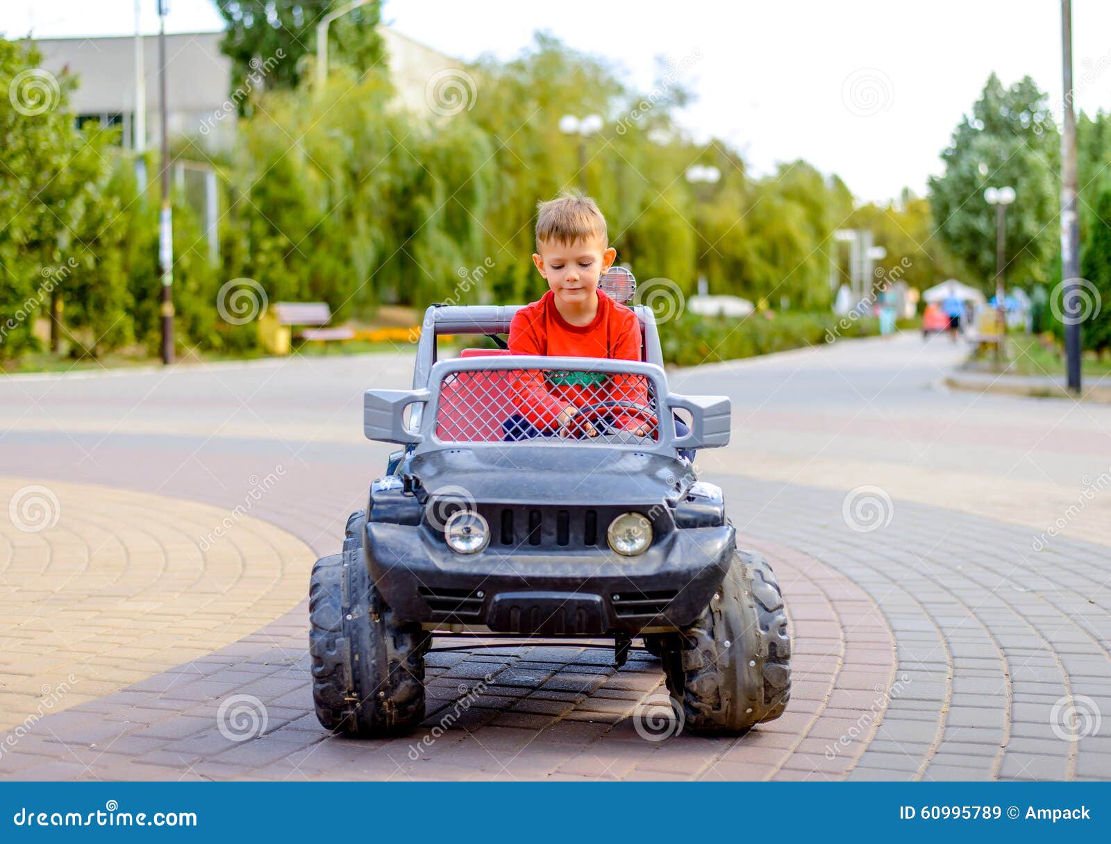 Netter kleiner Junge, der einen Spielzeuglastwagen fährt. Der nette kleine Junge, der einen großen mechanischen Spielzeuglastwagen dreht das Lenkrad mit einem Blick der Konzentration als spielt er fährt, in einem Stadtpark