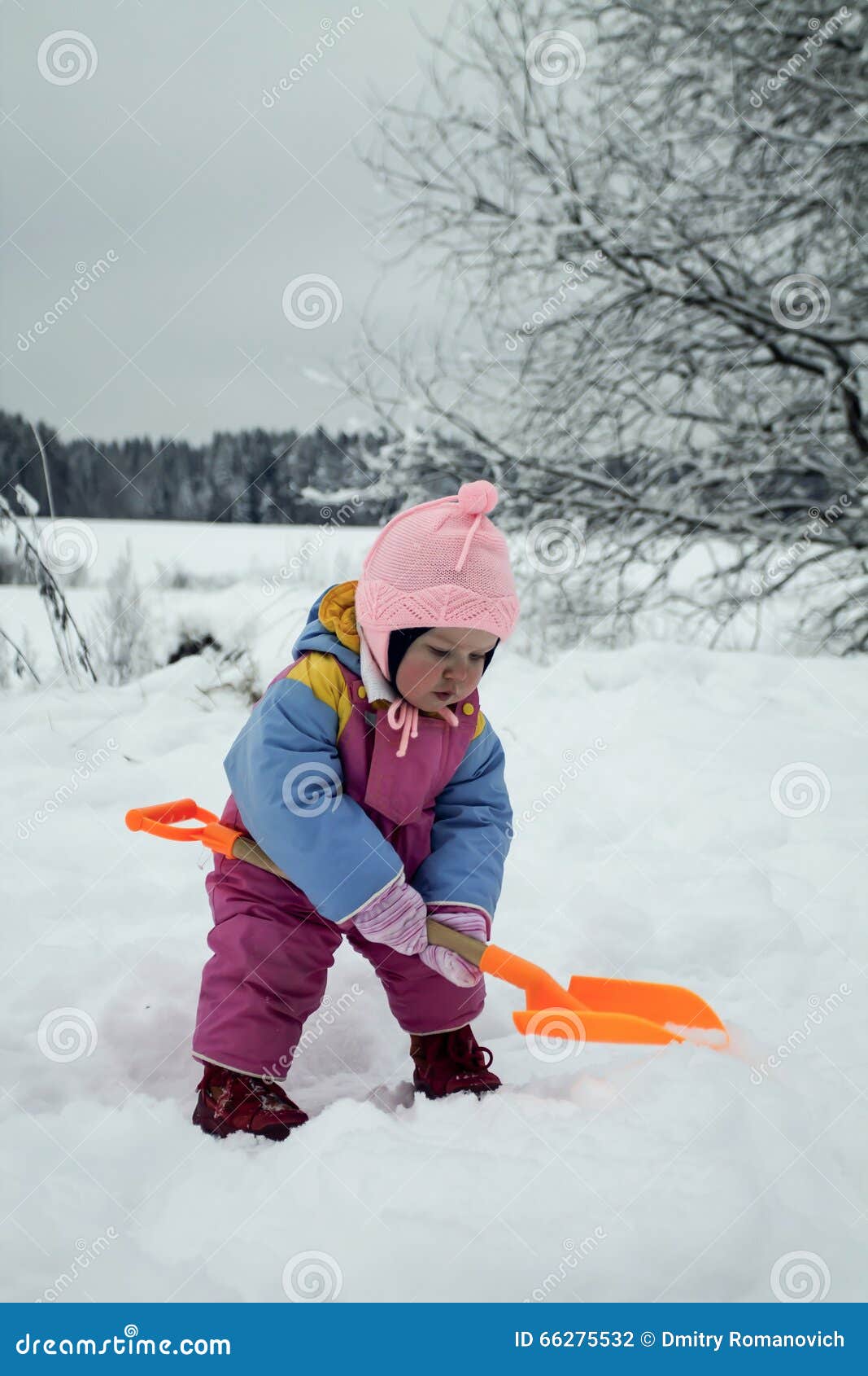 Neve de escavação da menina com Toy Shovel. A menina está andando no dia de inverno, ela está escavando a neve com a pá alaranjada do brinquedo em suas mãos