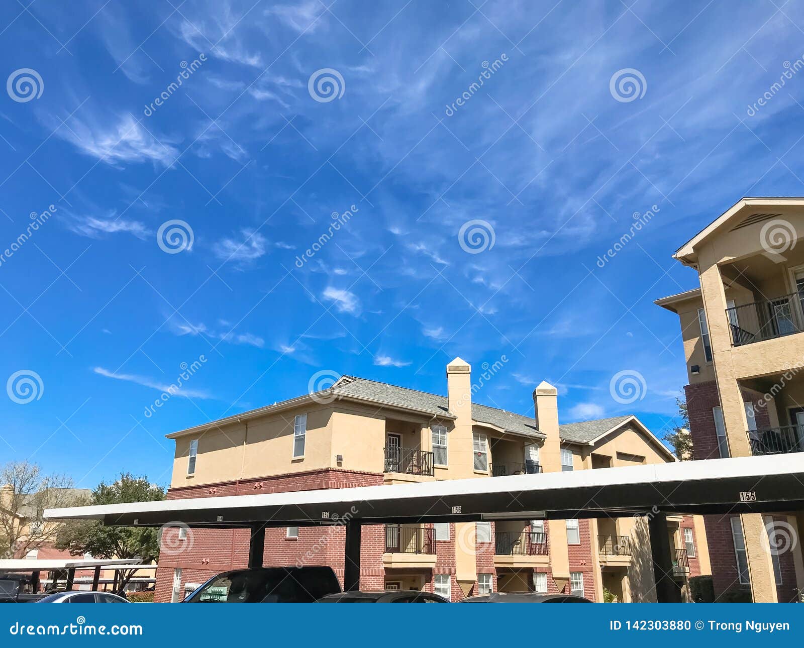 New Apartment Complex with Covered Parking Under Sunny Cloud Sky in