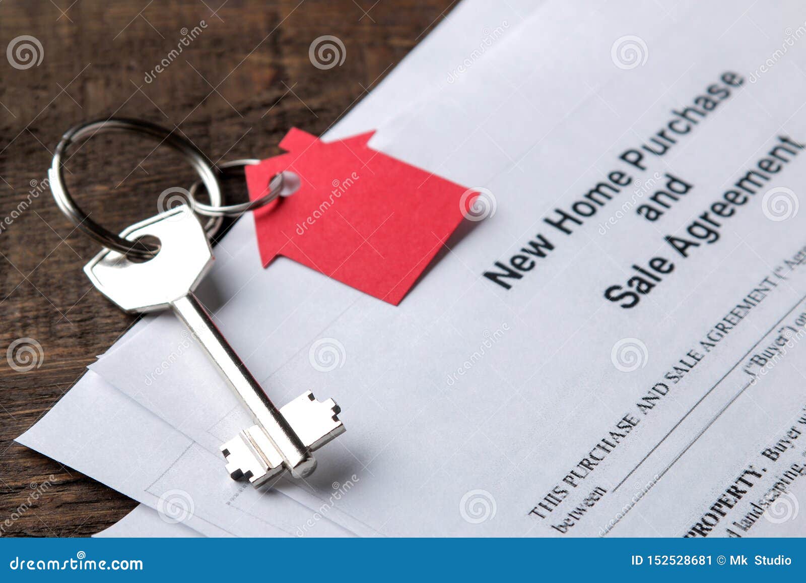 new home purchase and sale agreement. key with keyring and blank on a brown wooden table. concept of buying a home