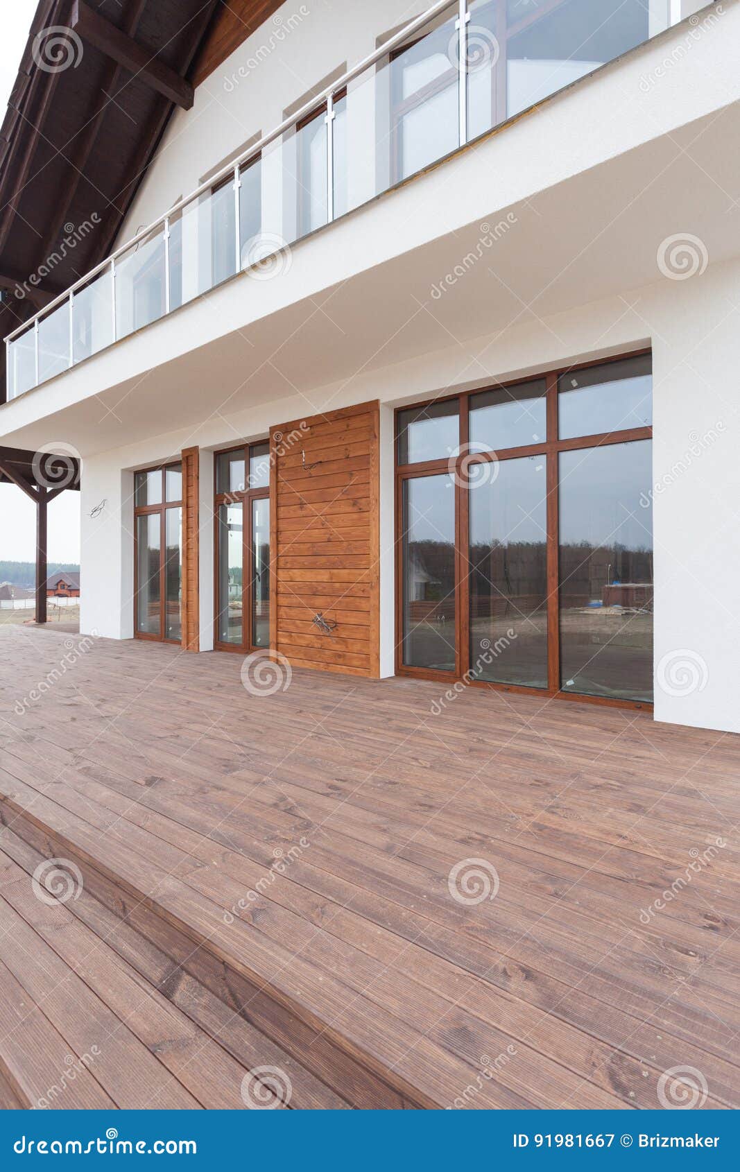 new house with white walls, wooden terrace and glass balcon.