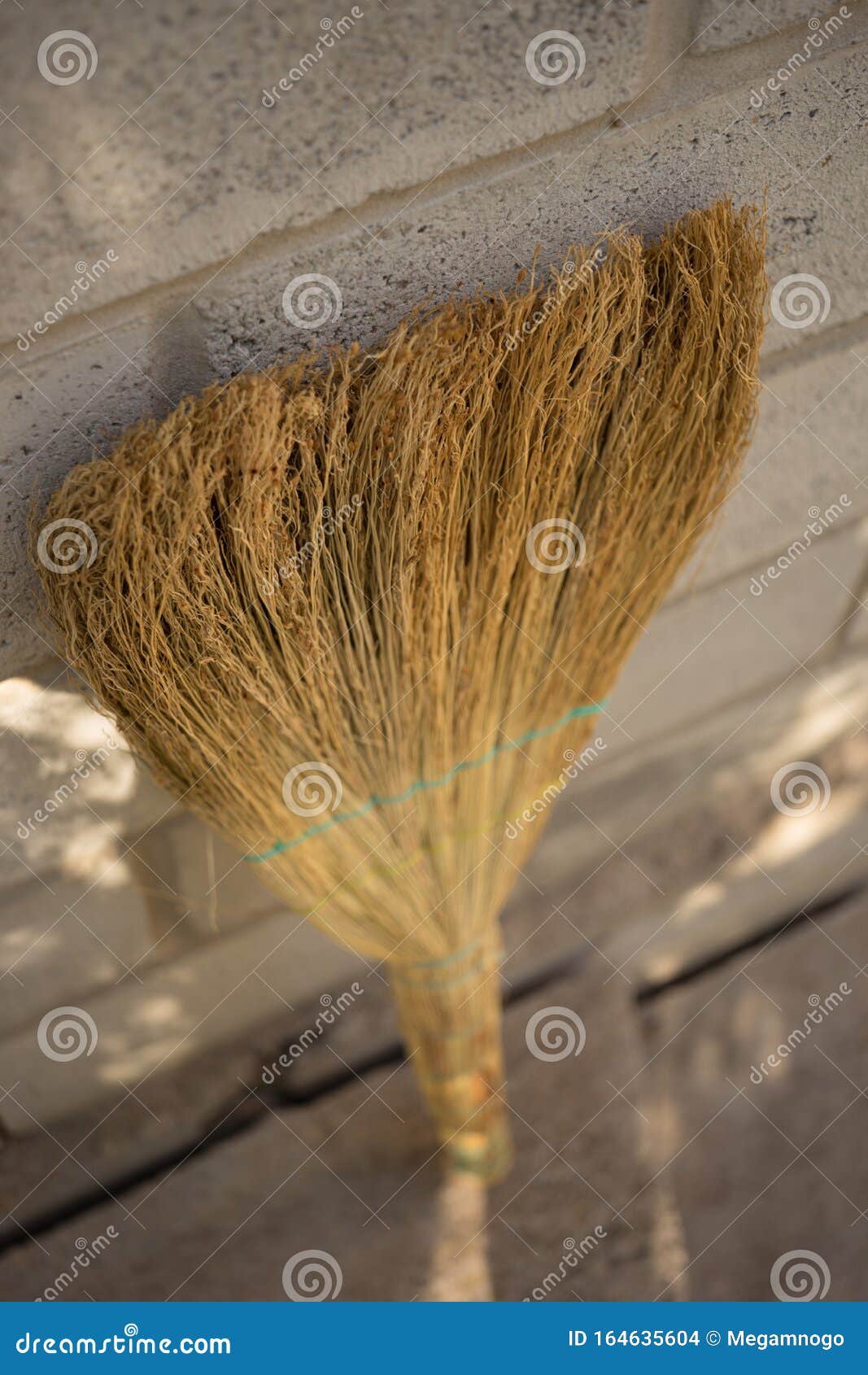 A New Wicker Broom Stands Upside Down Against the Wall Stock Photo