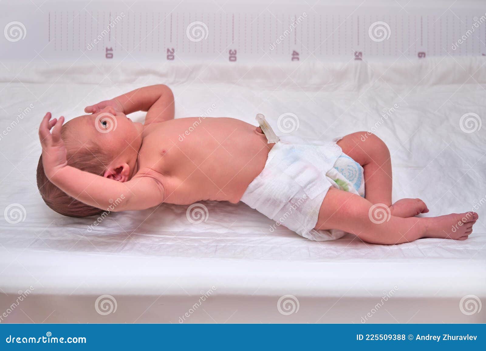 a newborn baby in diapers on a white changing table with a ruler for measuring full-length