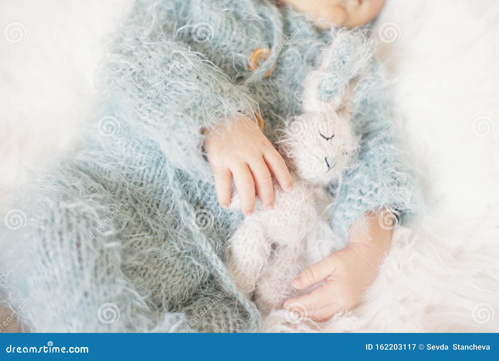 newborn baby. sleeping baby in bed, holding a bunny toy. baby with blue knitted romper