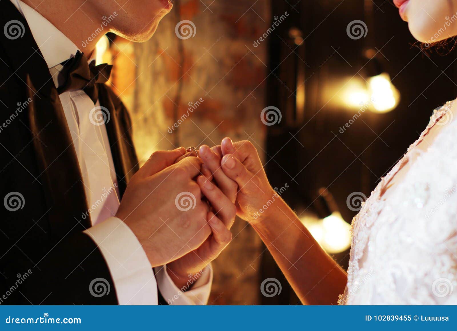 newlyweds exchange rings, groom puts the ring on the bride`s hand in marriage registry office. dark brown background