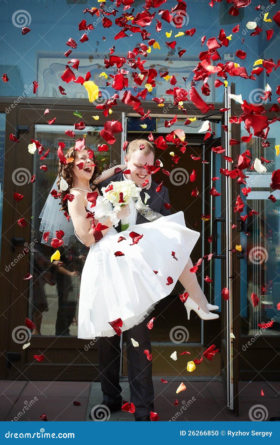 Newlyweds felizes noiva e noivo com pétalas. Newlyweds felizes e pétalas vermelhas e brancas do vôo