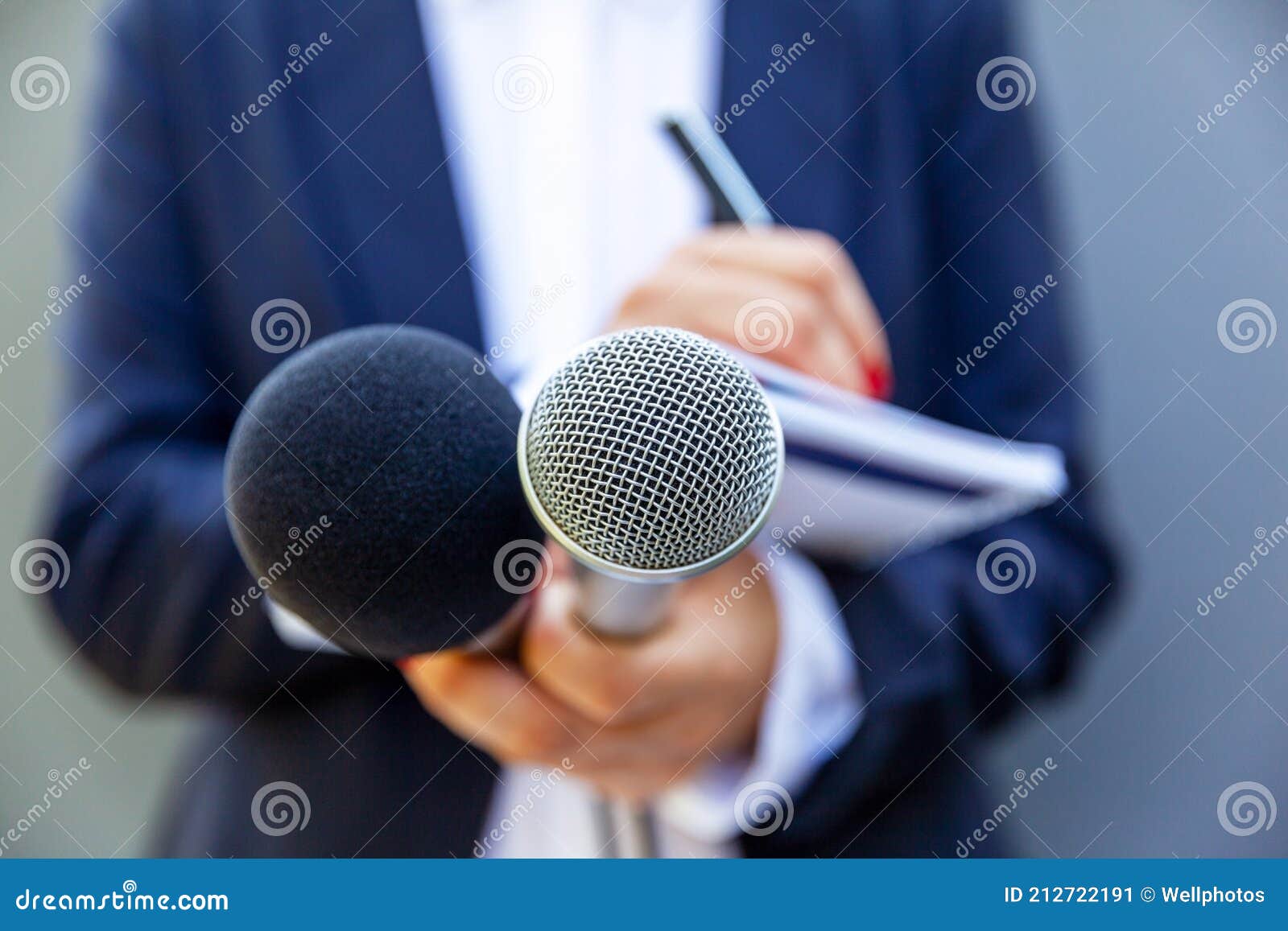 female journalist at news conference or media event, writing notes, holding microphone