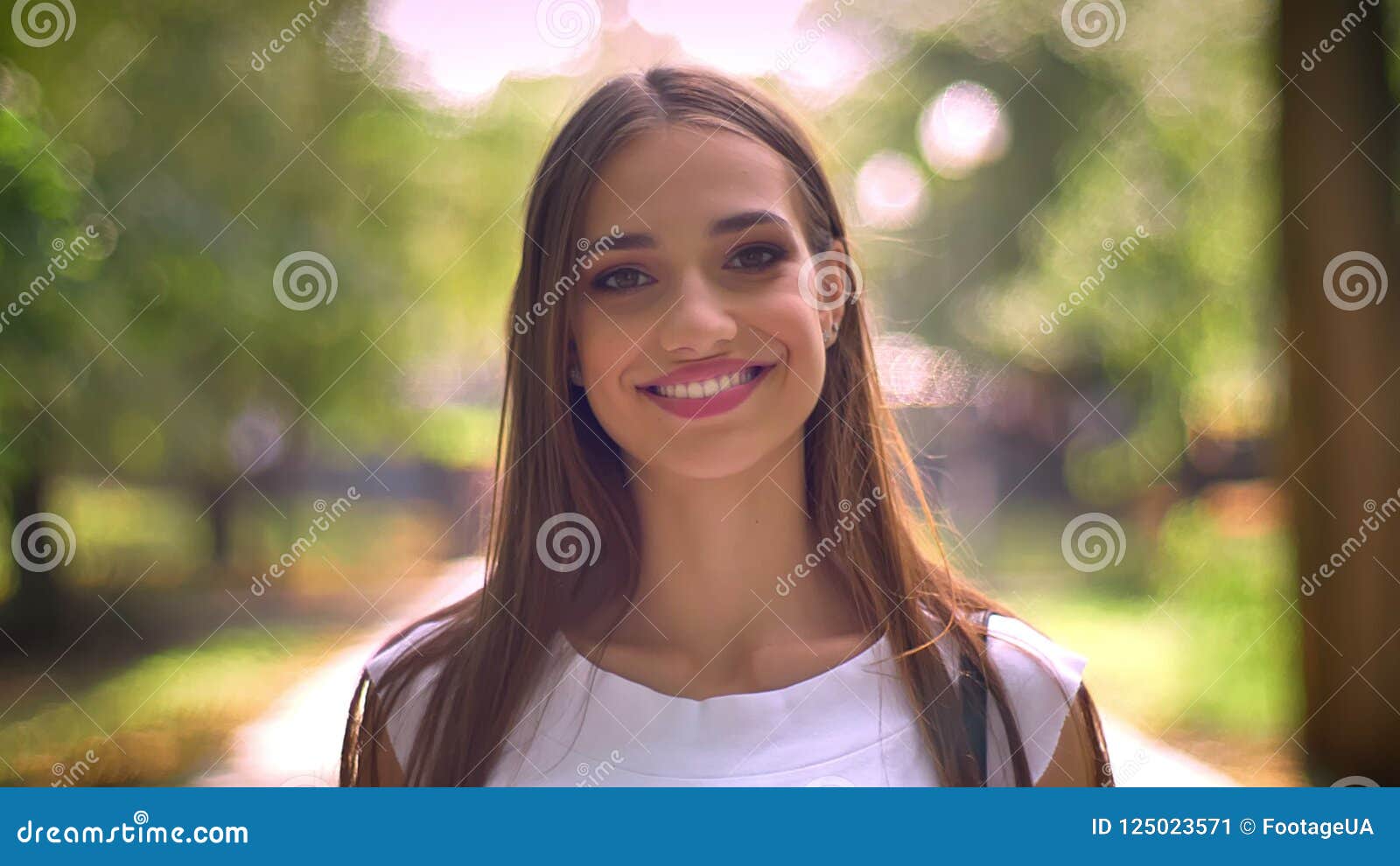 Portrait of pretty smiling teen girl wearing round glasses looking at  camera outdoors on blurred landscape background with copy space in spring  day. Stock Photo