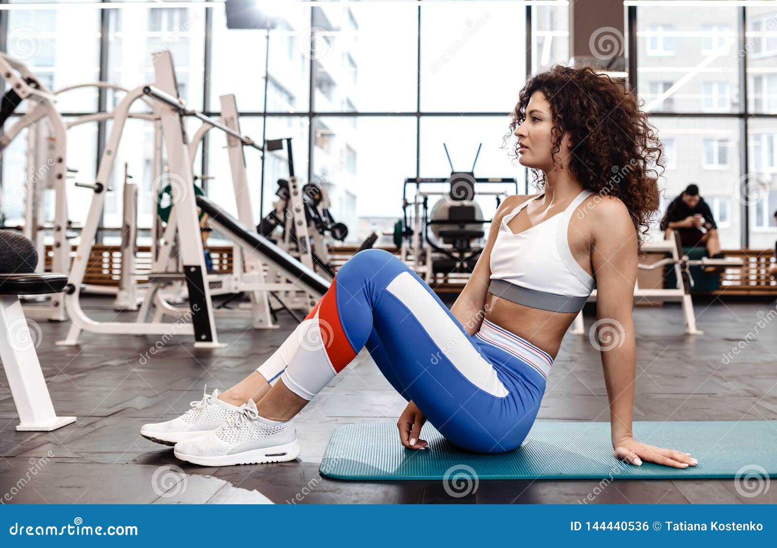 Nice Slim Curly Dark-haired Girl Dressed in Sports Clothes is Sitting on  the Mat for Fitness in the Modern Gym with a Stock Photo - Image of  beautiful, exercise: 144440536