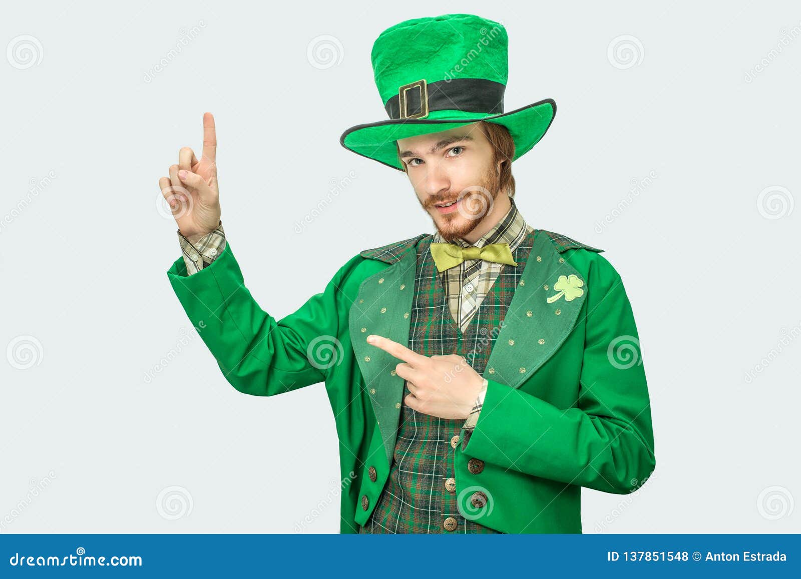 nice young man in green suit look on camera and point up. he wear sait patrick`s costume. on grey background.