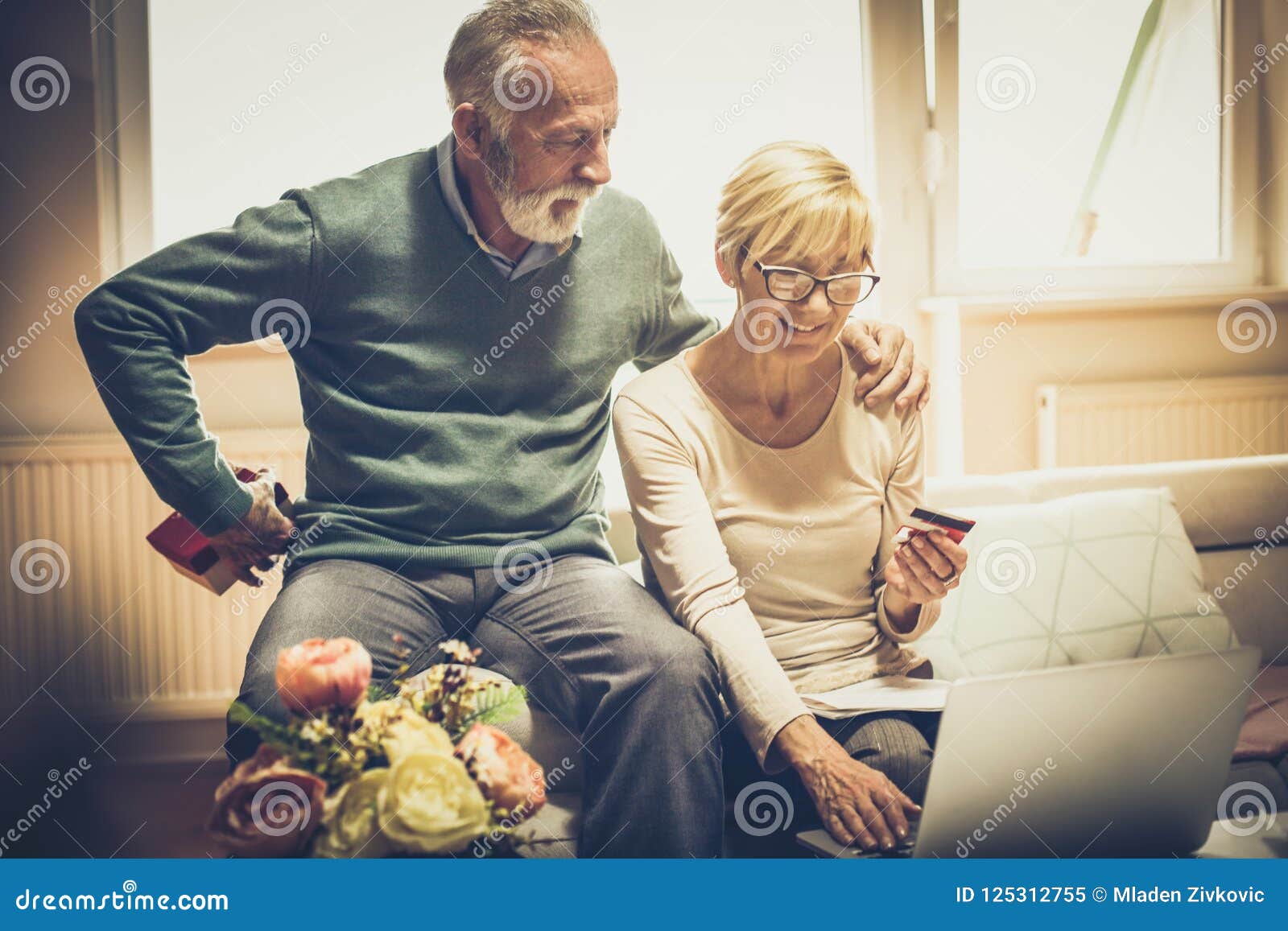 Niespodzianka powoduje uśmiech Starsza para z kredytową kartą i laptopem w domu Starsi mężczyzna trzyma prezent dla jego żony