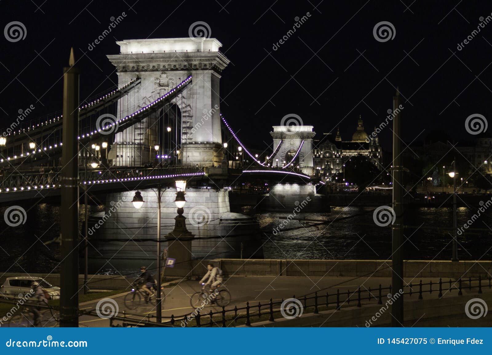 night view of the chain bridge with cyclists walking the streets of budapest, hungary