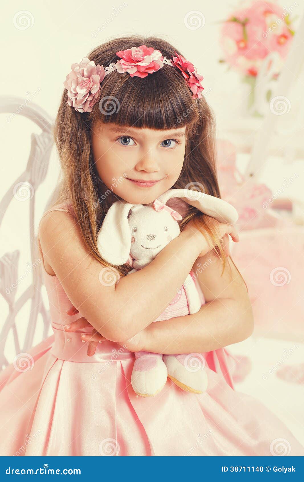 Niña con el juguete suave que se sienta en una silla. Una niña bonita en el vestido blanco, sentando en el taburete su conejo de la felpa