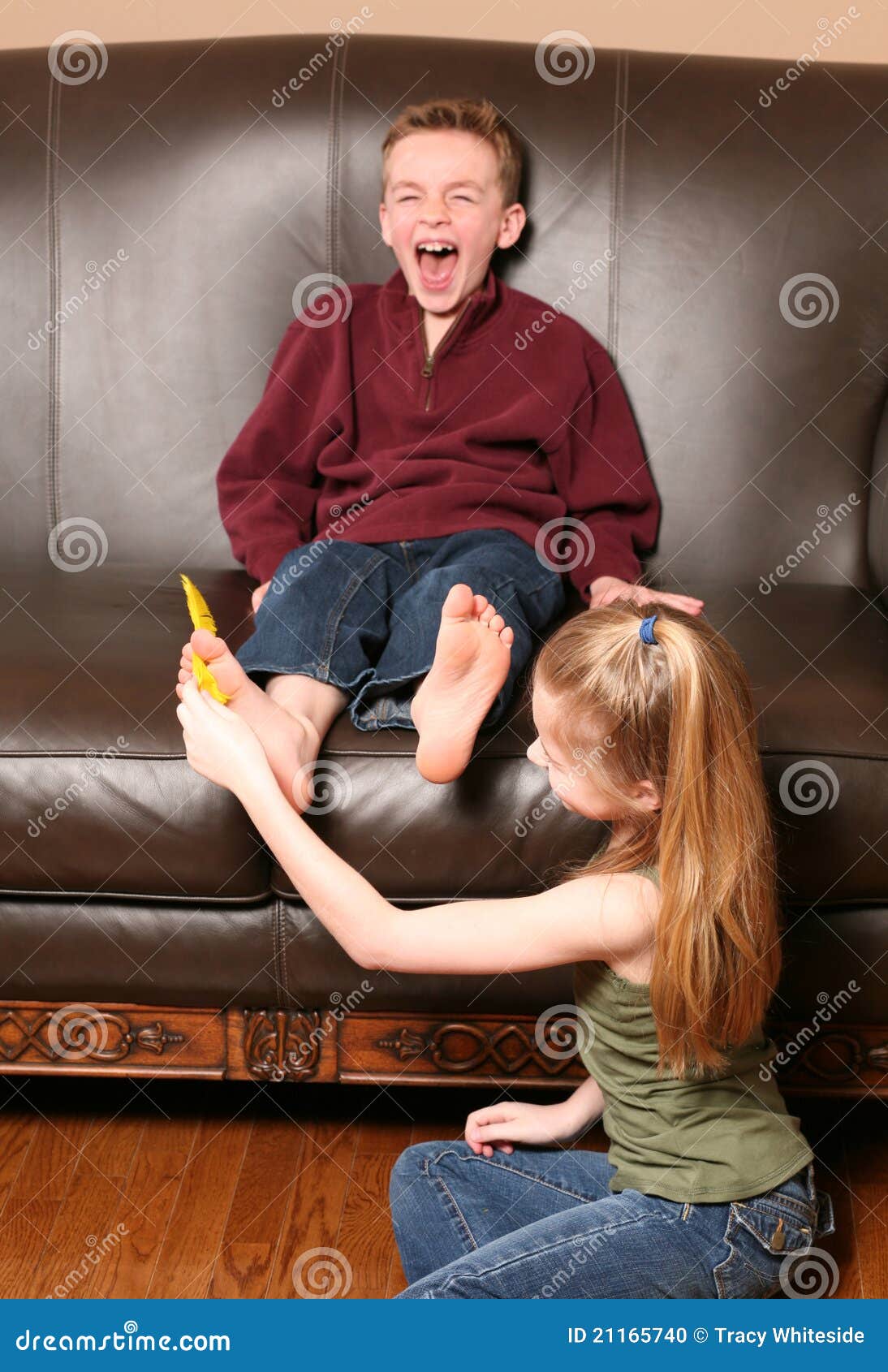 Niños que cosquillean pies con la pluma. Niña linda que cosquillea los pies del muchacho con las plumas