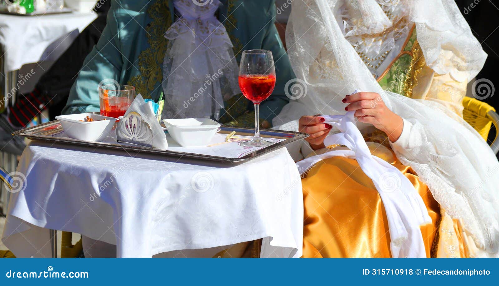 noble couple from venice wearing old clothes from the last century while drinking an alcoholic spritz at the alfresco table