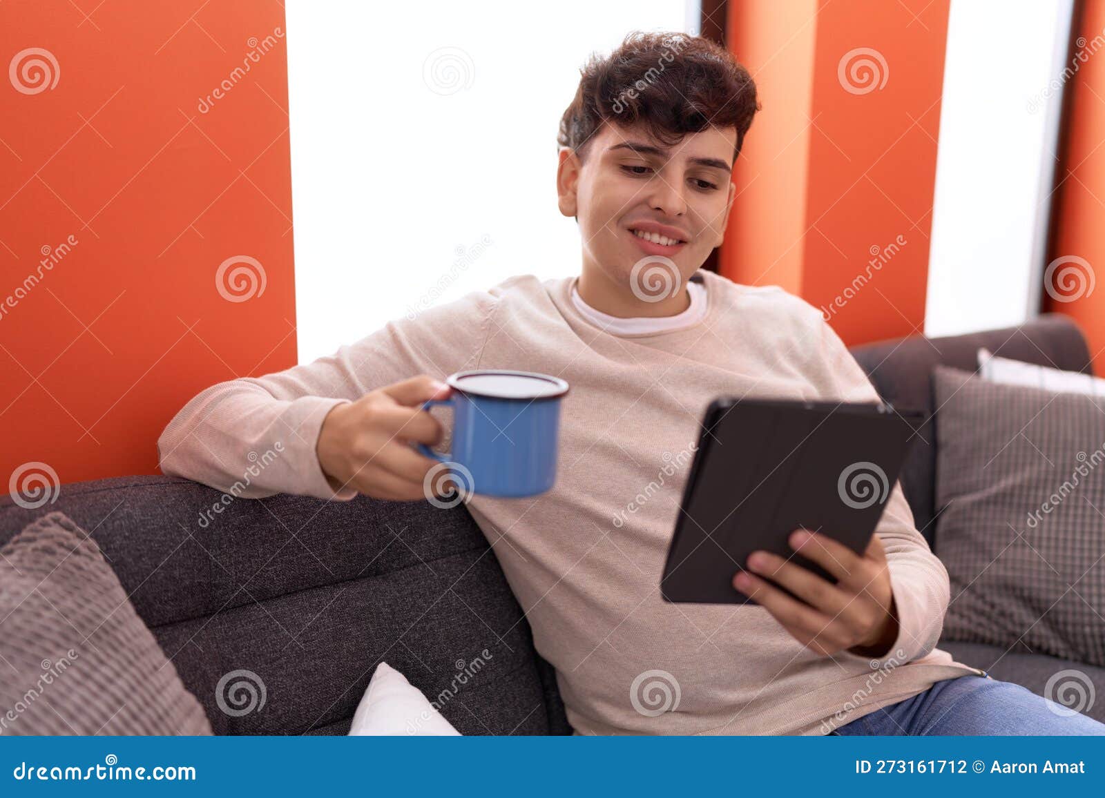 non binary man using touchpad drinking coffee sitting on sofa at home