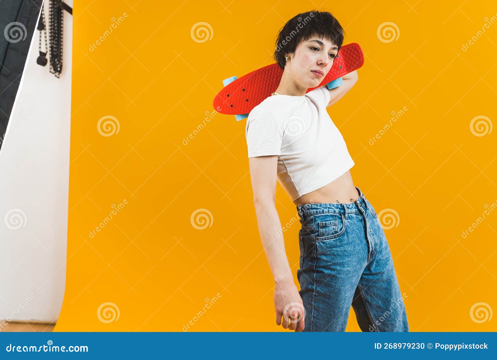 non-binary model positing with small skateboard in studio over yellow background. promotion of sport and outdoor