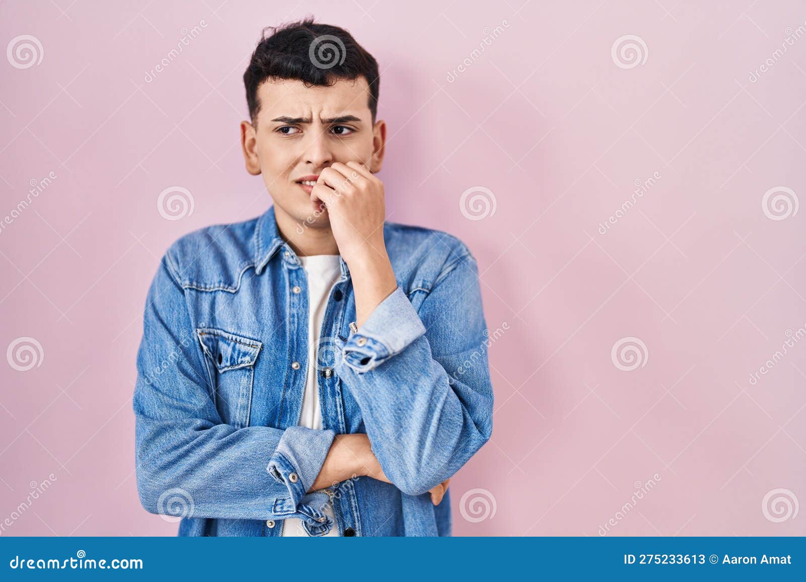 non binary person standing over pink background looking stressed and nervous with hands on mouth biting nails