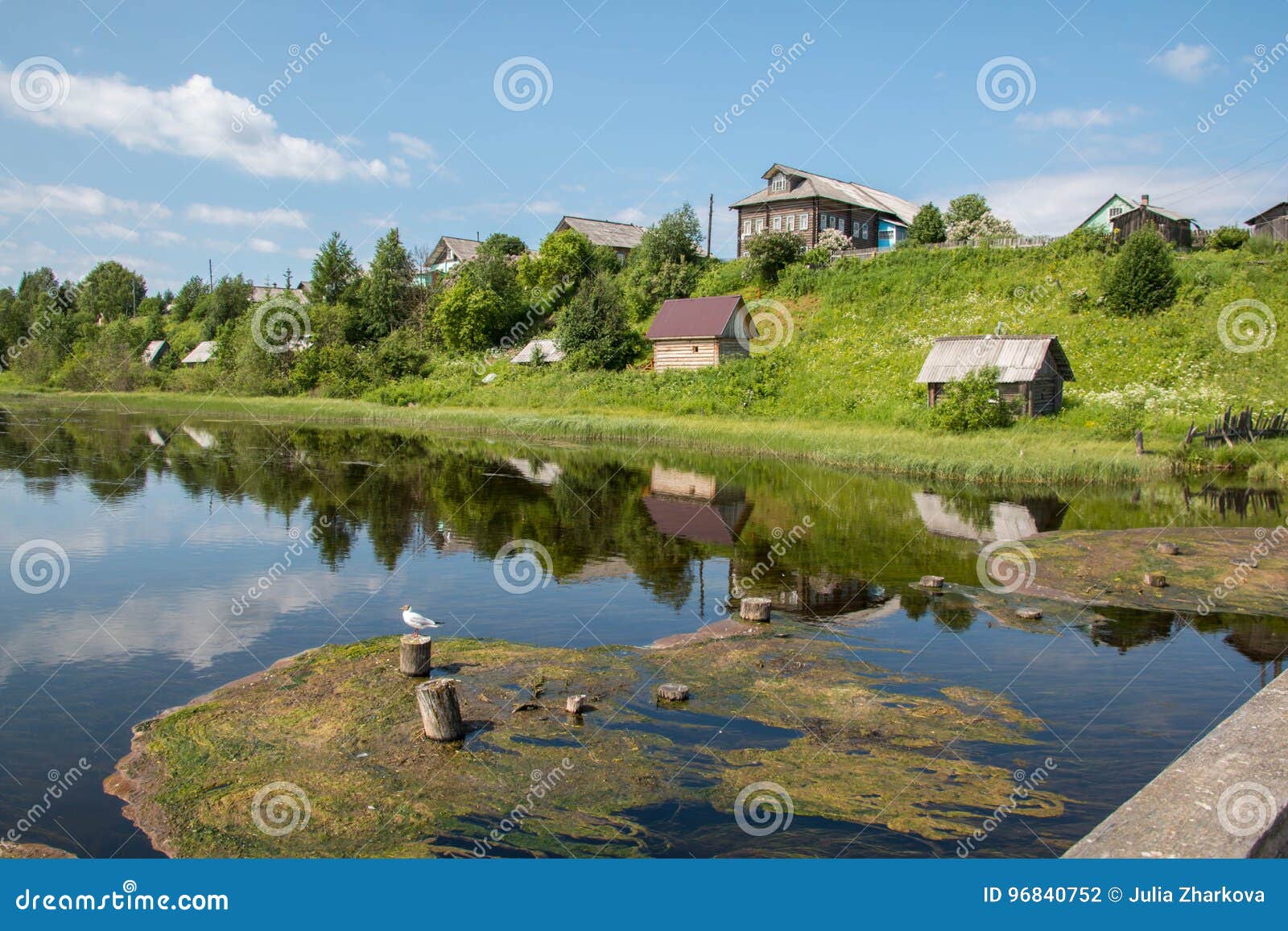 north russian village isady. summer day, emca river, old cottages on the shore, old wooden bridge and clouds reflections.