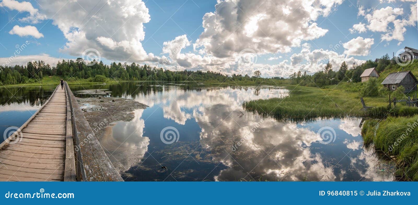 north russian village isady. summer day, emca river, old cottages on the shore, old wooden bridge and clouds reflections.