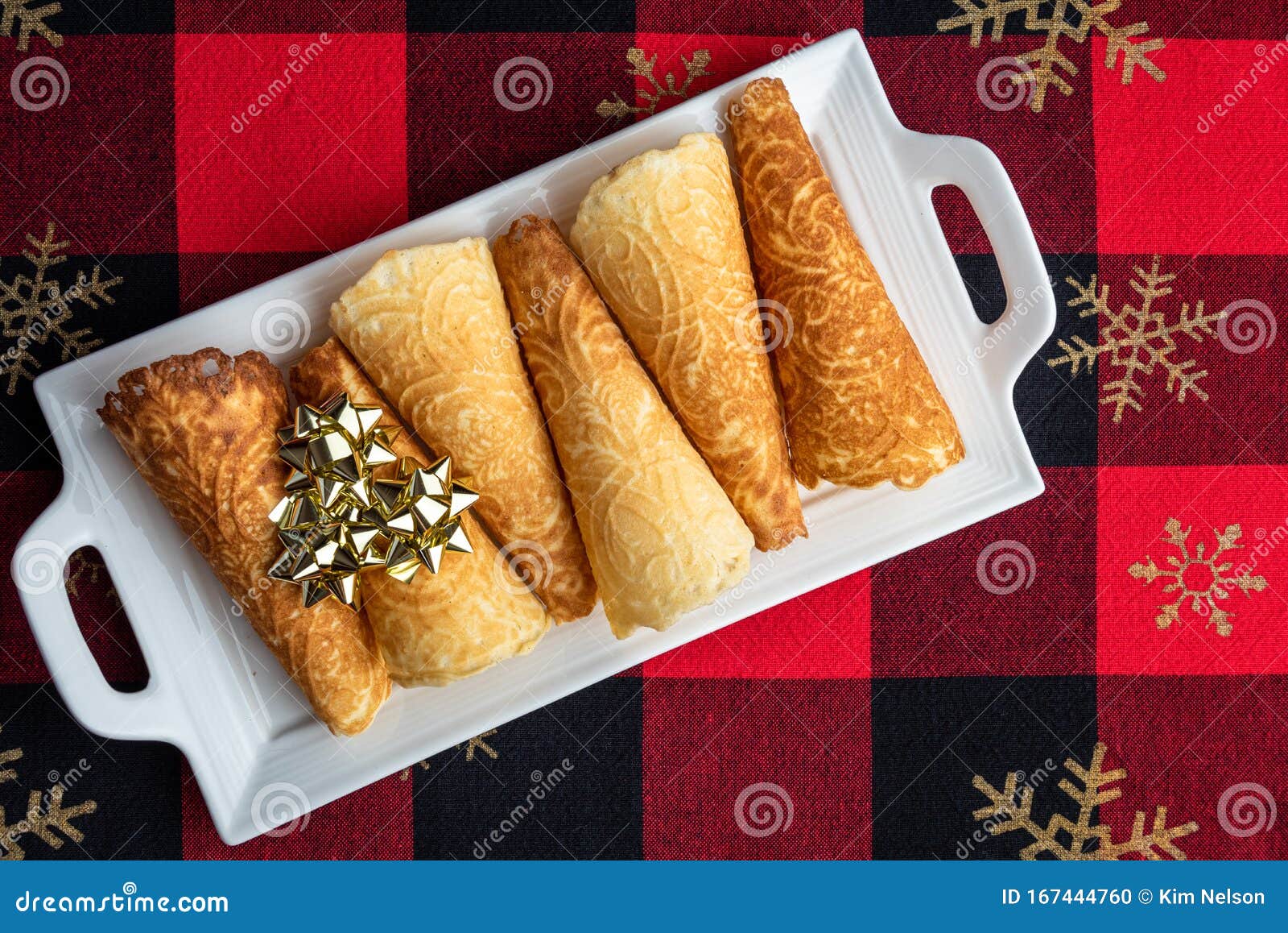 norwegian krumkake cookies on a white ceramic plater, red and black tablecloth with gold snowflakes, gold ribbon bows