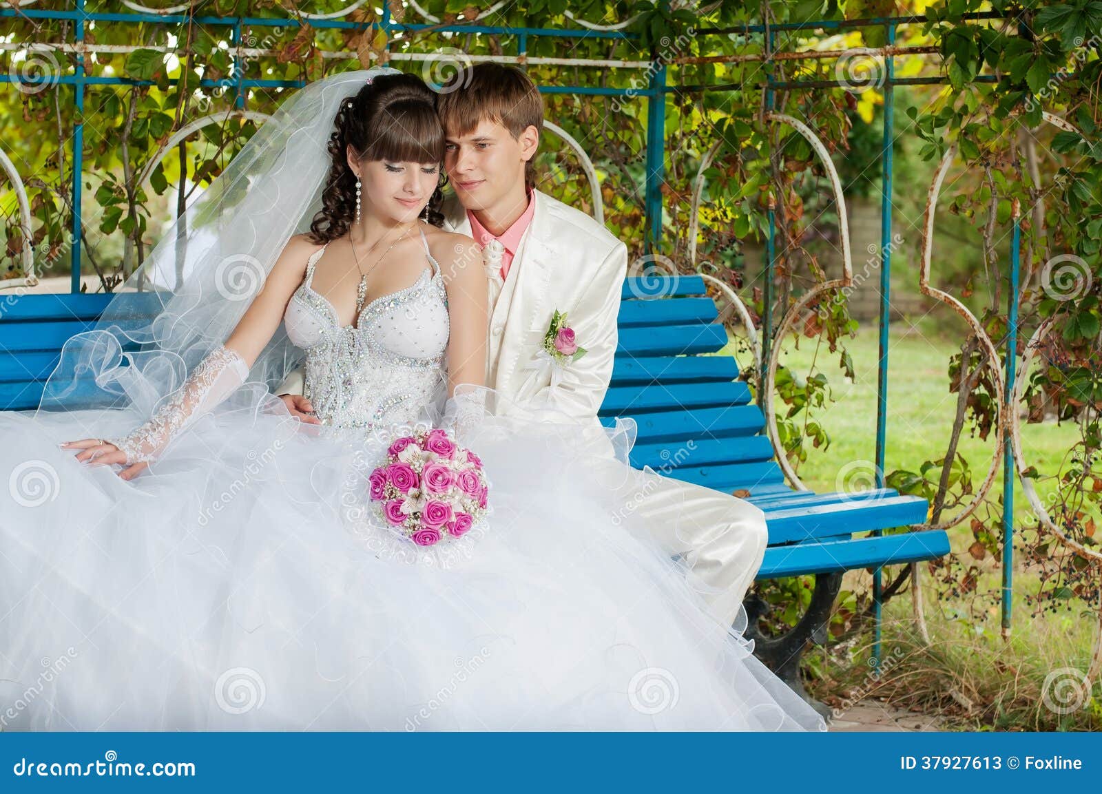 Novia y novio jovenes y hermosos en el banco en el jardín