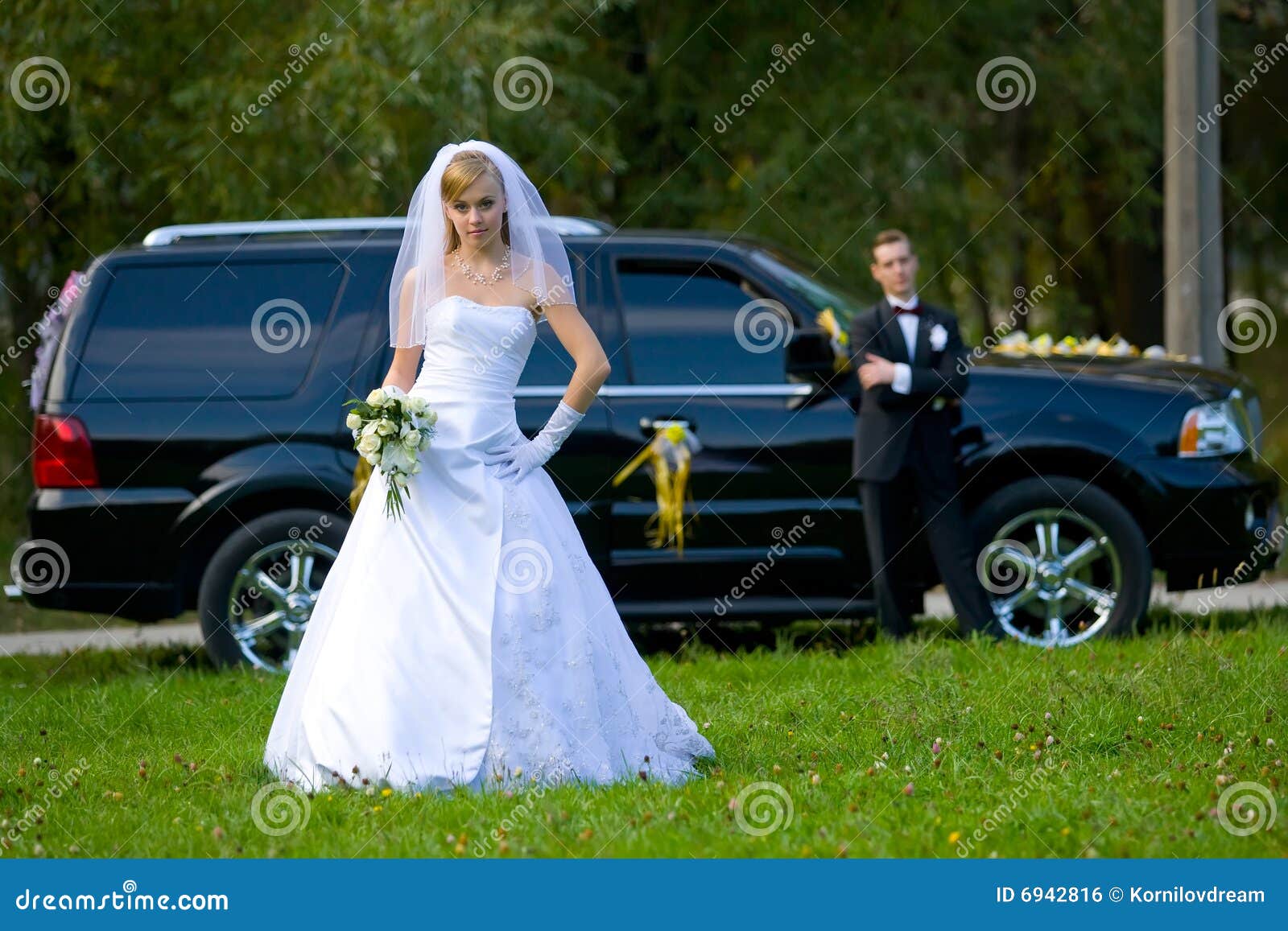 Novia y novio que se colocan delante del coche negro de la boda